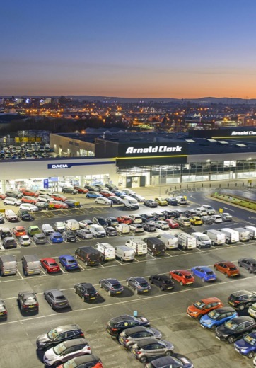 Arnold Clark Head Office in Hillington pictured from above with the forecourt at the front and Glasgow in the background against a sunset sky.
