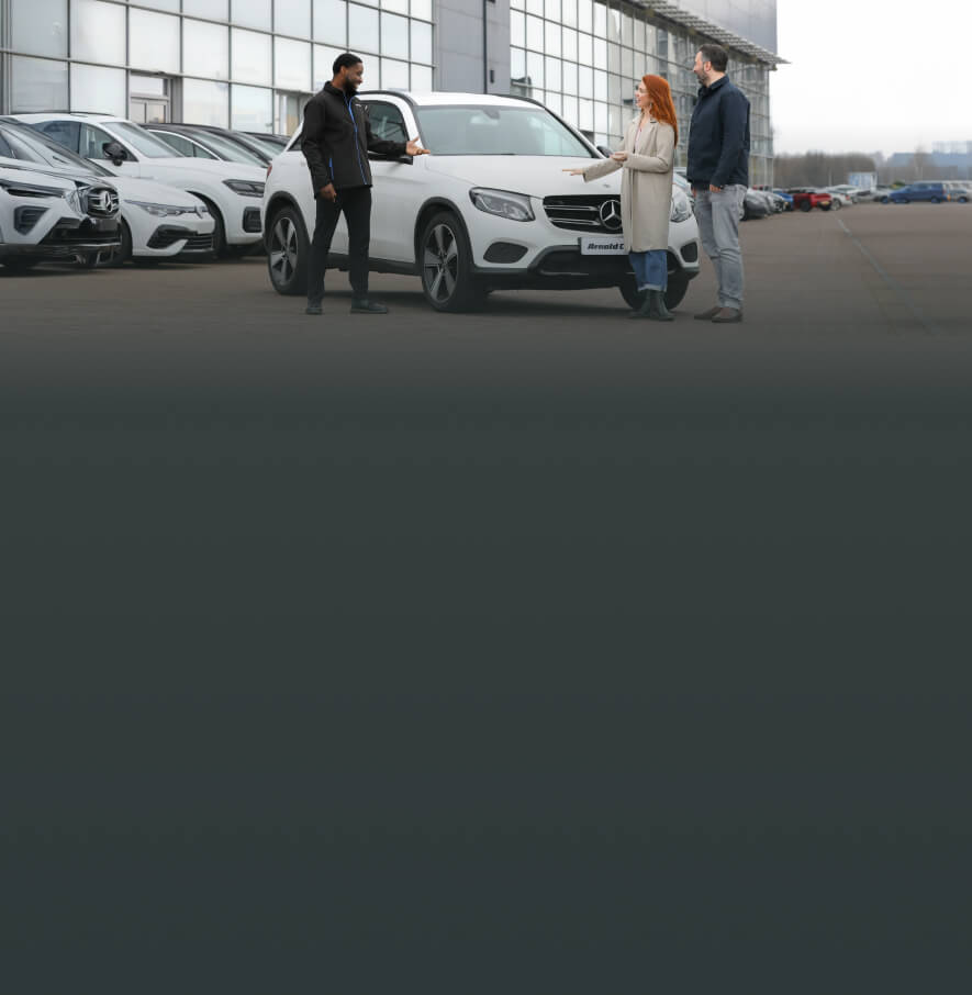 Three people having a conversation in front of a white Mercedes-Benz SUV with a car dealership forecourt in the background