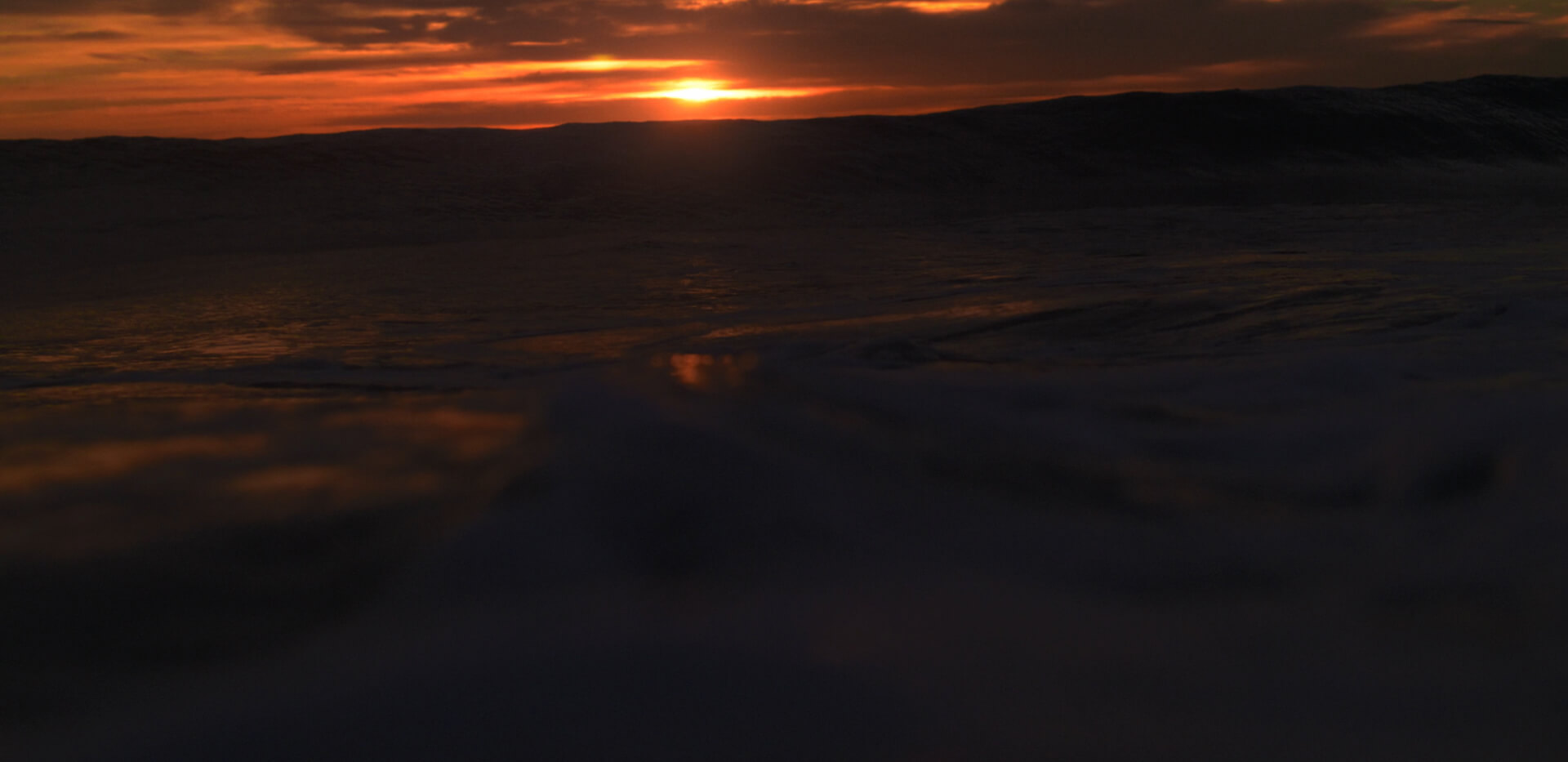 Sunset over dark ocean waves with an orange and red sky
