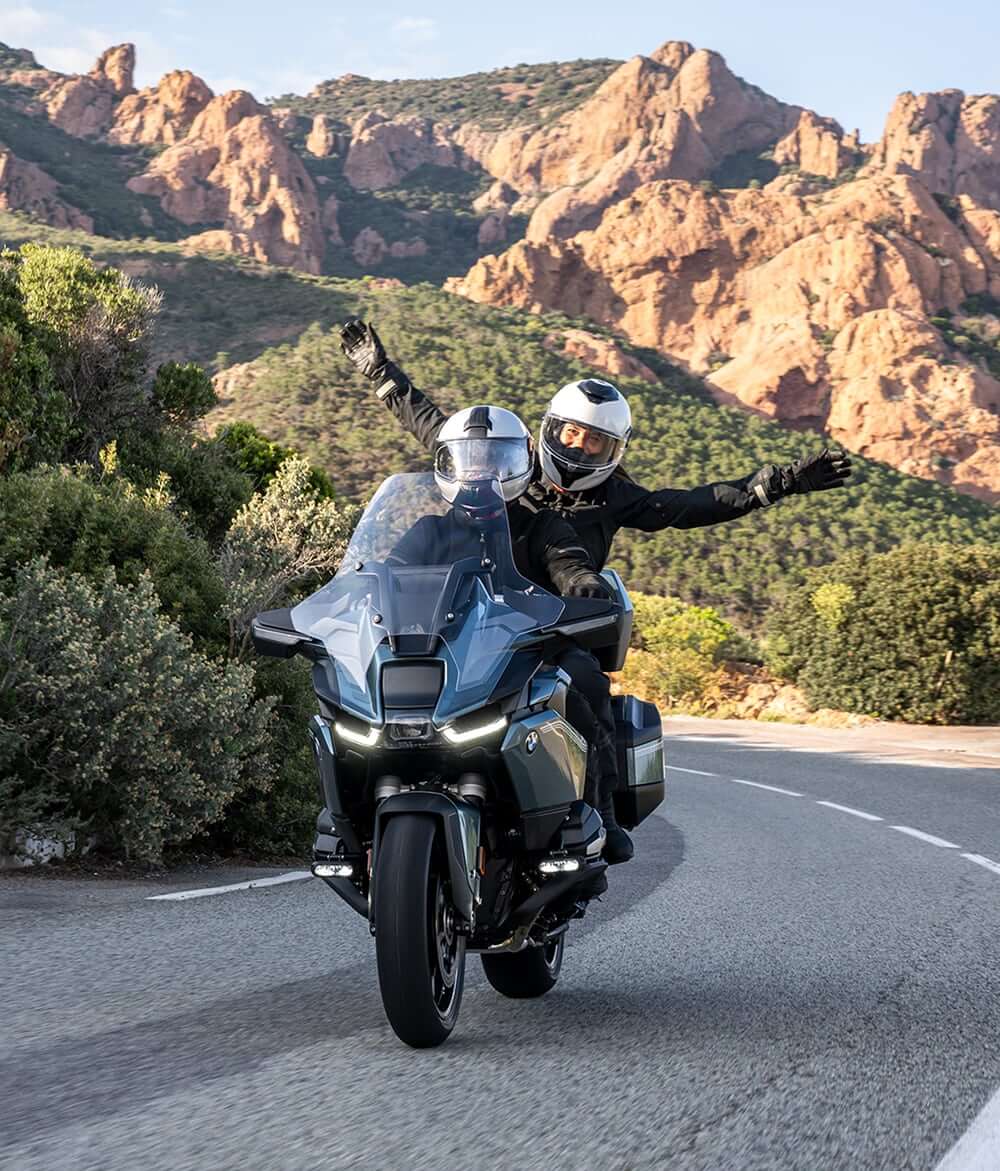 Two people riding on the road with a BMW motorcycle with rear passenger hands in the air