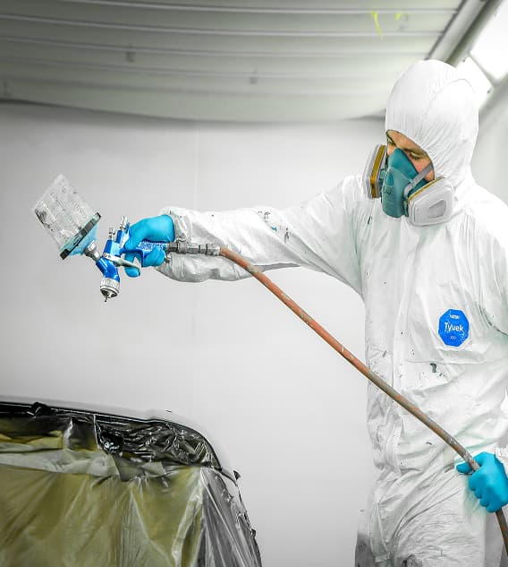Staff member in overall using spray painter gun on vehicle