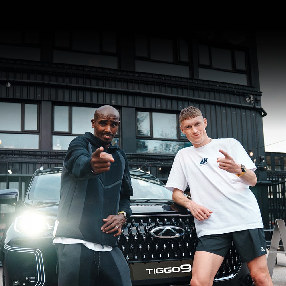 Mo Farah and Adam Clarke standing infront of a Chery Tiggo 9 with it's lights on