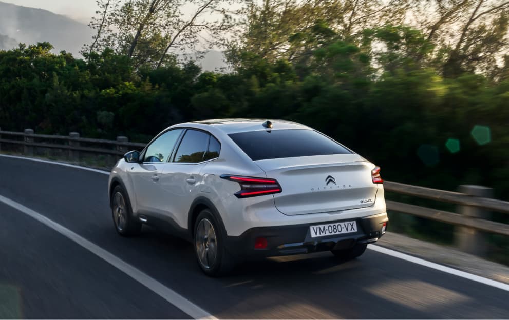 View of the rear end of a white Citroen C4 X driving down a road.
