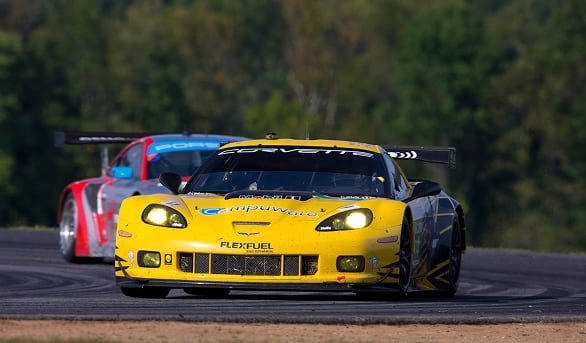 Yellow Corvette race car leads a red race car on a curved track with a blurred forest background