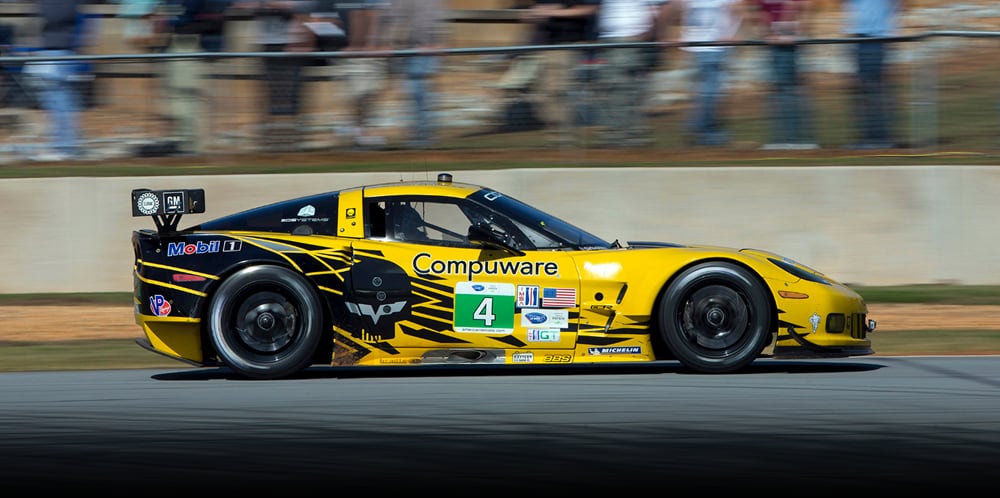 Side view of yellow Corvette race car speeding on a race track