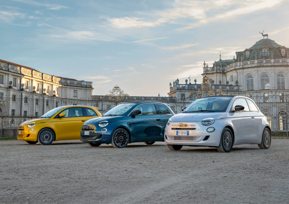 Front side angled view of Fiat 500 vehicles parked with histroric building in background