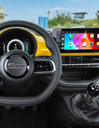 Interior view of a Fiat 500 Hybrid showing the steering wheel, digital dashboard, touchscreen infotainment system, and manual gear stick