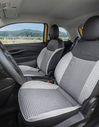 Interior view of a Fiat 500 Hybrid showing front seats with black and gray patterned upholstery and a scenic landscape visible through the window.