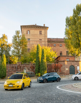 Front anngled side view of Fiat 500 Hybrid vehicles driving with a historic building in the background
