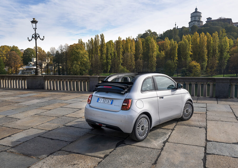 Rear angled view of Fiat 500 Hybrid convertible with parked with historic building background