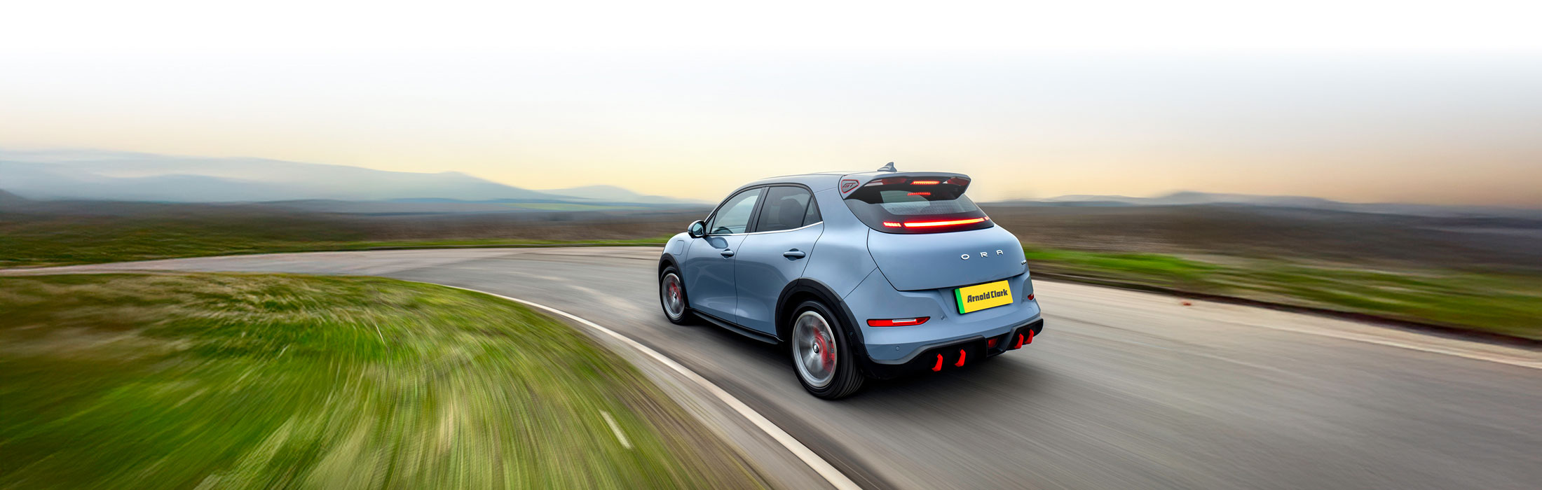 Rear view of a red GWM ORA 03 on a city street at night with headlights on