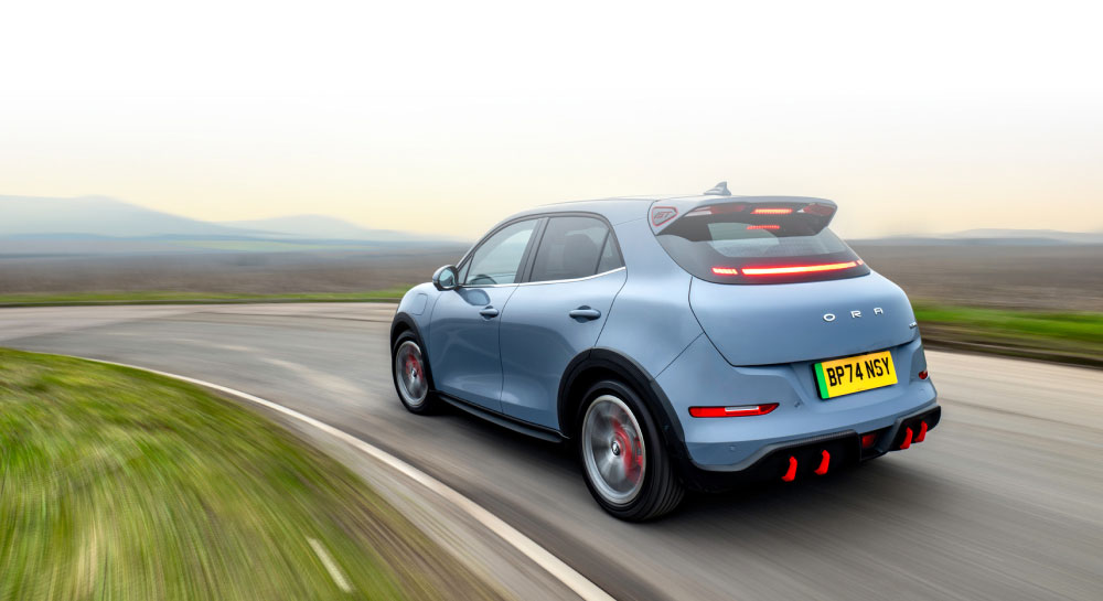 Rear view of a red GWM ORA 03 on a city street at night with headlights on