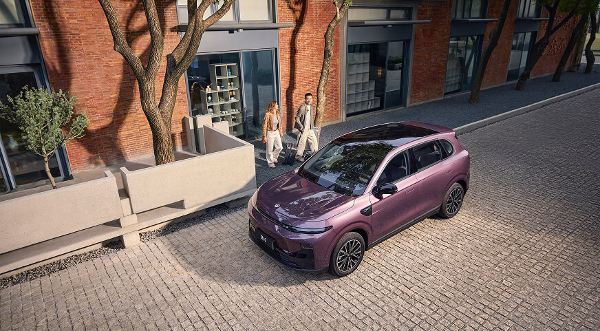 A purple Leapmotor B10 parked on a cobblestone street outside a modern brick building with two people walking nearby