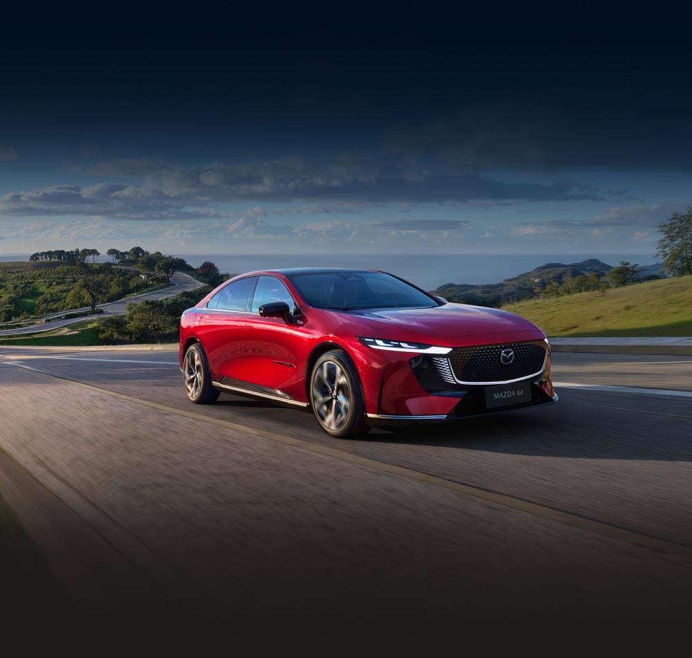 Red Mazda6e travelling along coastal road in the sun