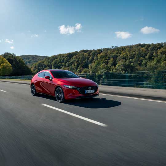Red Mazda 3 driving on road