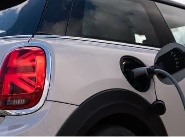 Rear angled shot of a MINI's tail light and fuel cap open, plugged into charge.