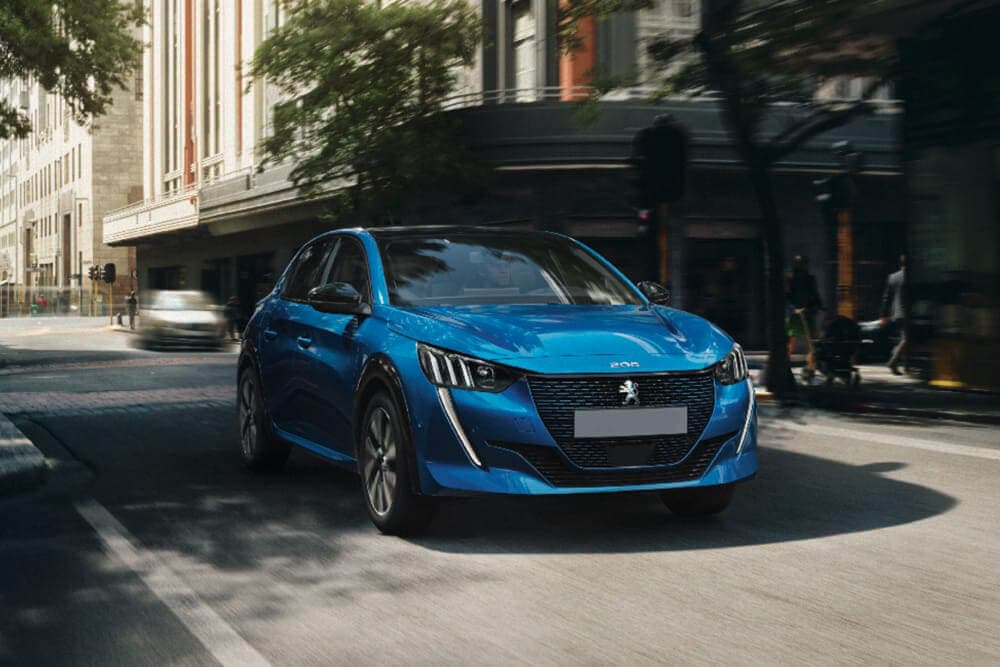 Peugeot e-208 driving down a street.