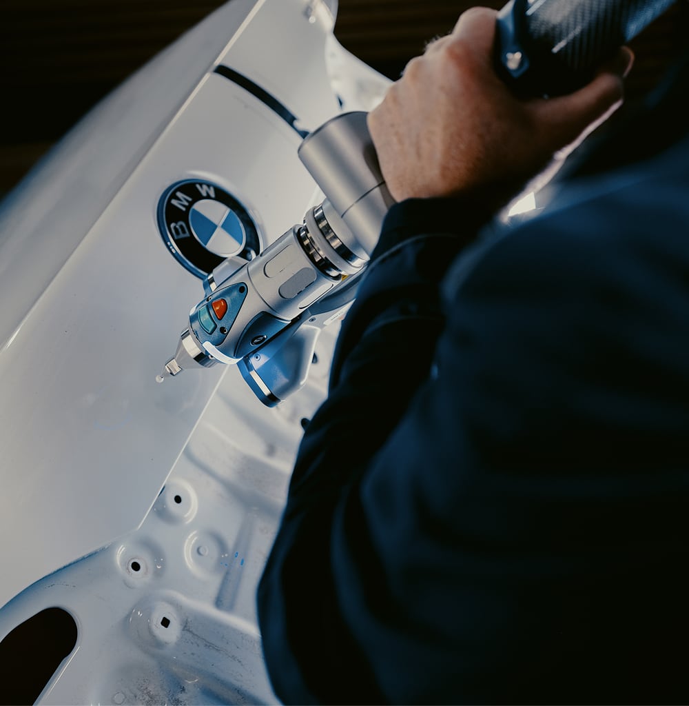 Person using a handheld tool to repair or inspect BMW vehicle panel close-up