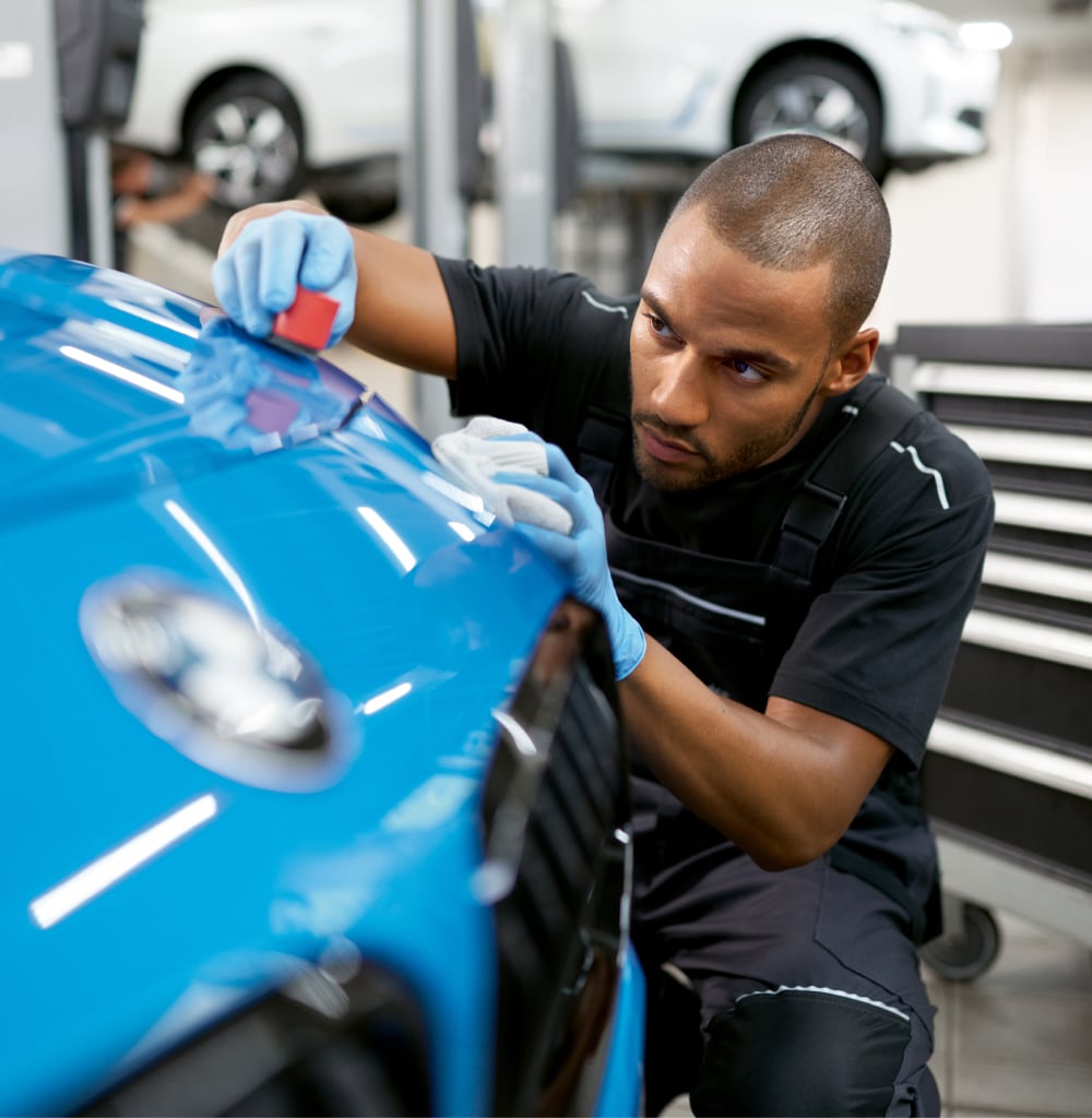 Man in gloves carefully polishing the hood of a blue BMW car in a workshop