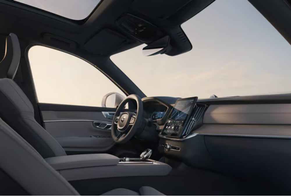The interior of a Volvo vehicle, showing the driver's seat, steering wheel, dashboard, infotainment screen, panoramic sunroof and dashcam.