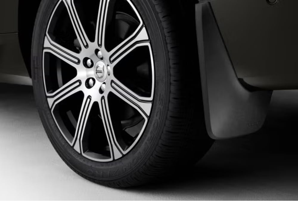 Close-up of a car wheel with a black and silver alloy rim and a black tire, showing a black mudguard behind the wheel
