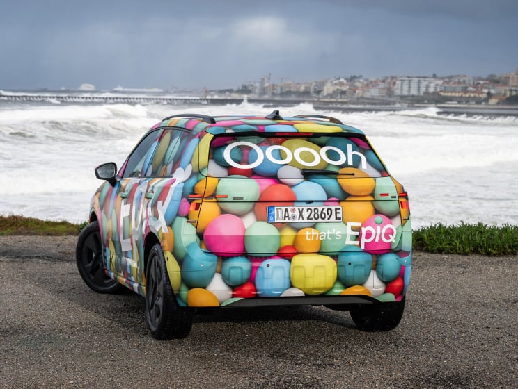 Rear angled view of Skoda Epiq with ocean and city buildings background