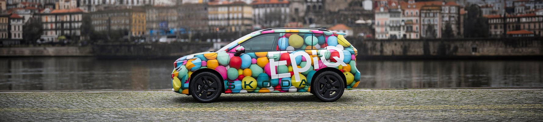 Side view of Skoda Epiq with river and city buildings background