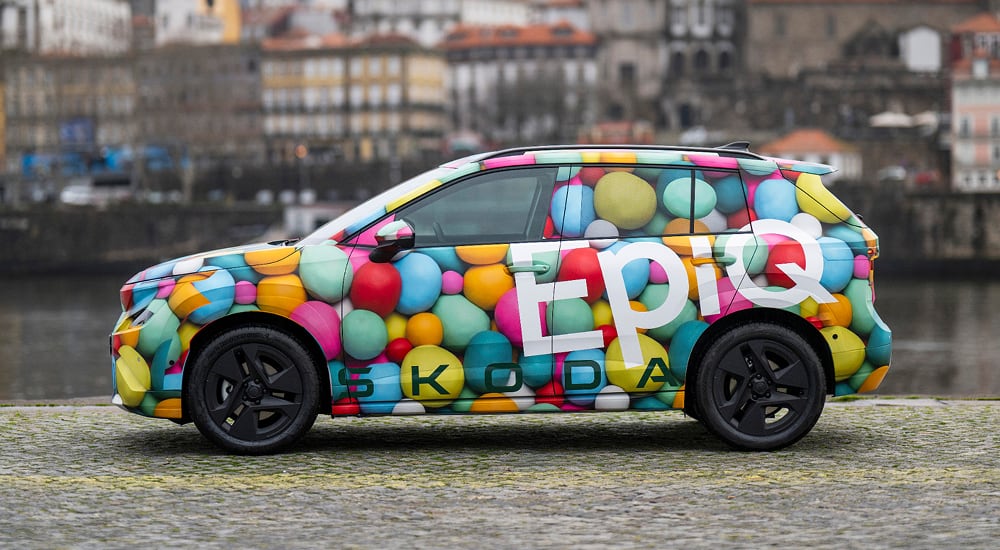 Side view of Skoda Epiq with river and city buildings background