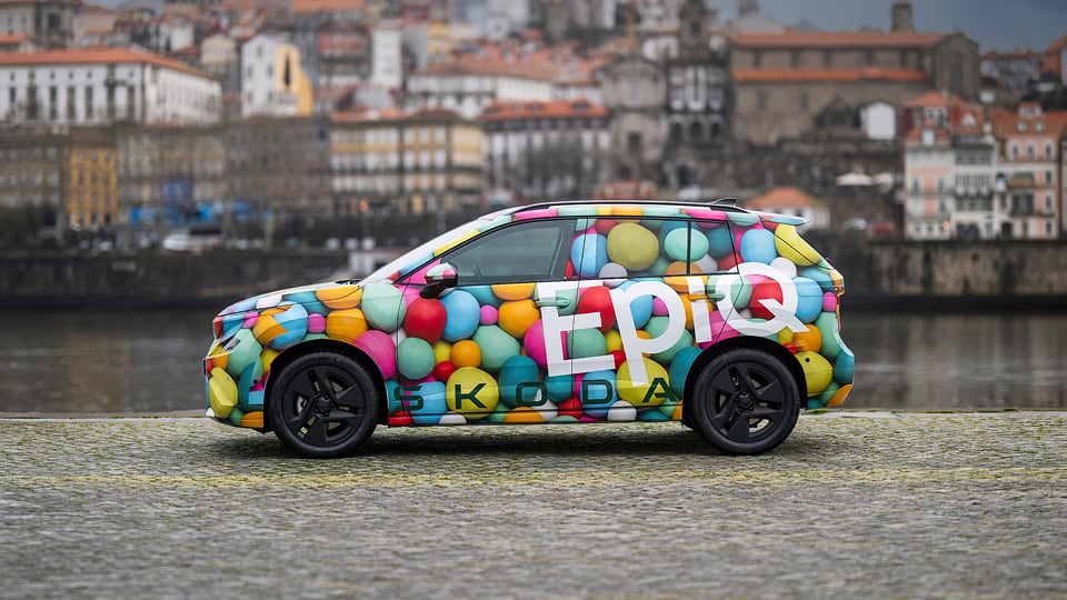 Side view of Skoda Epiq parked with river and city buildings background