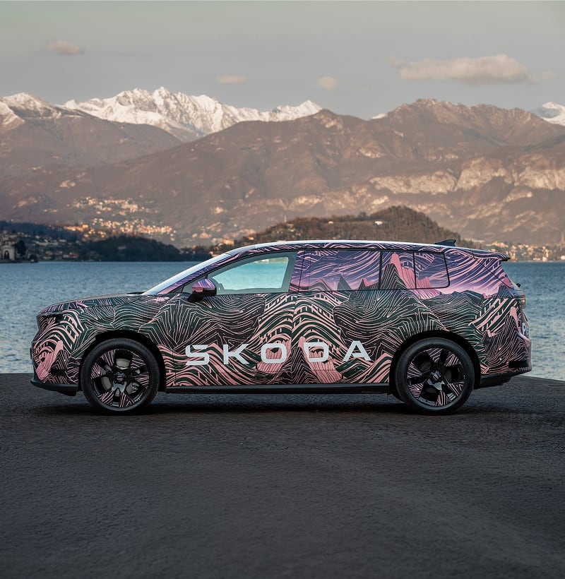 Side view of a Skoda Peaq parked with mountain and lake in the background