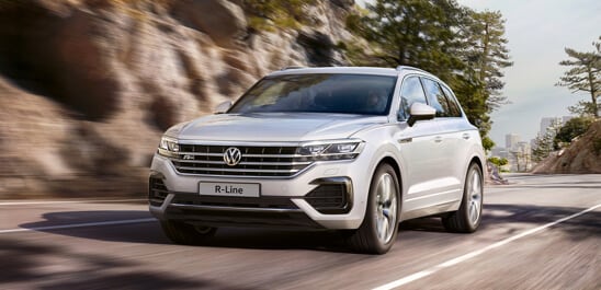 Silver Volkswagen Touareg driving down a mountain road.